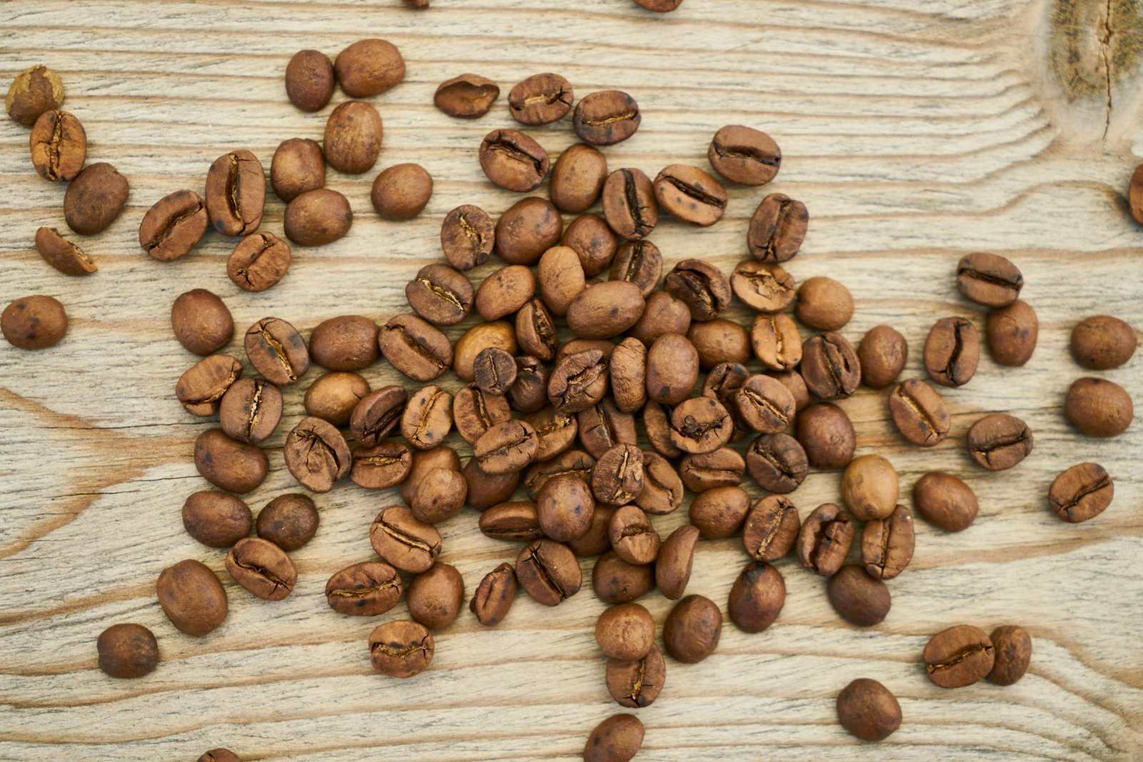 High-quality image of roasted coffee beans scattered on a wooden surface in a flat lay style.